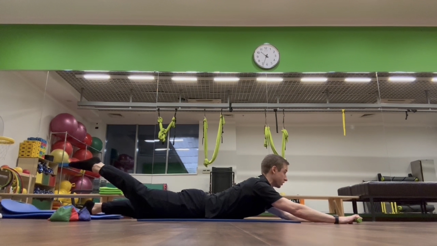 Гиперэкстензия на полу с движением лопаток и разгибанием бедра (в руках палка)