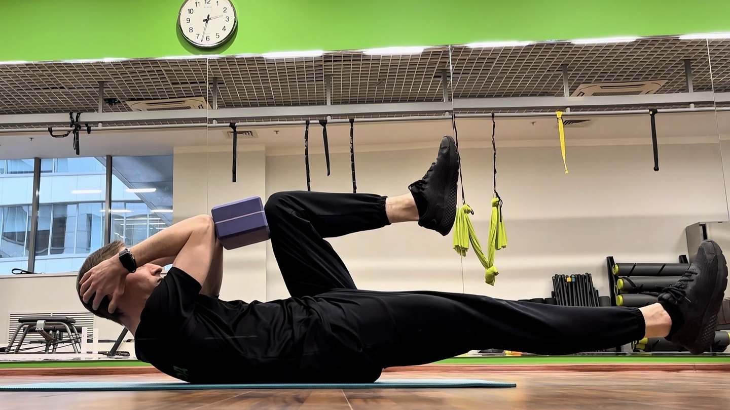 Сгибания ног с кирпичиком для йоги зажатым между локтями и коленями (вариация мертвого жука)